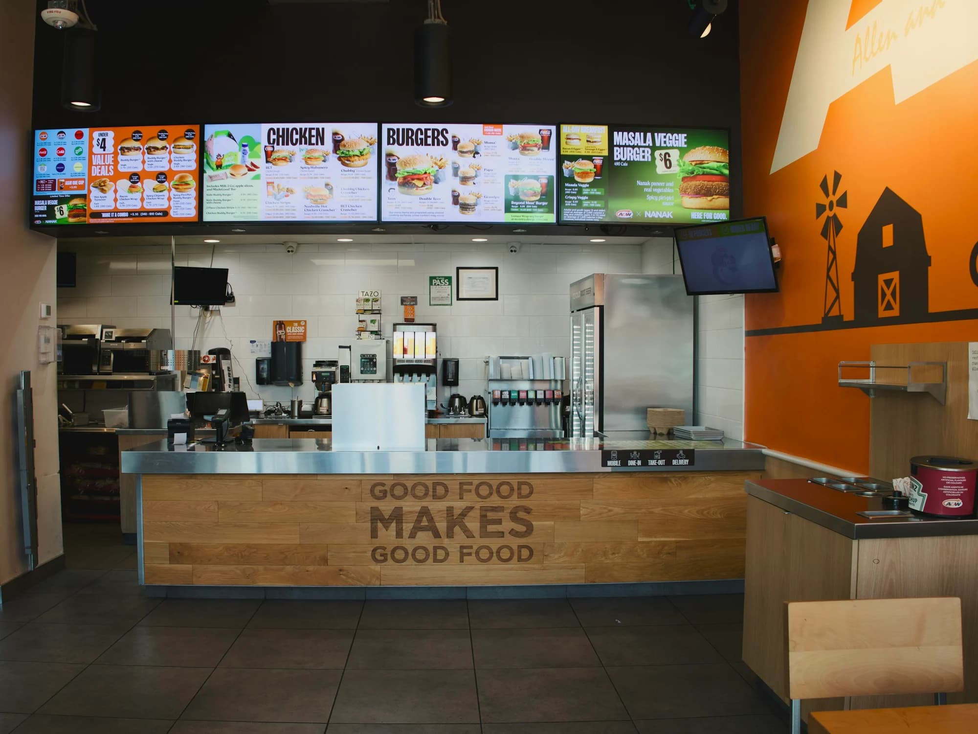 A quick-service restaurant counter with a row of digital menu screens overhead.