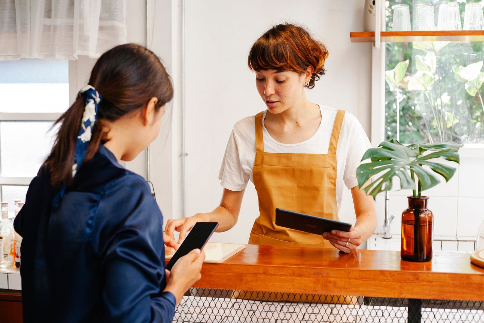 Two cafe colleagues discussing a phone and tablet at the counter